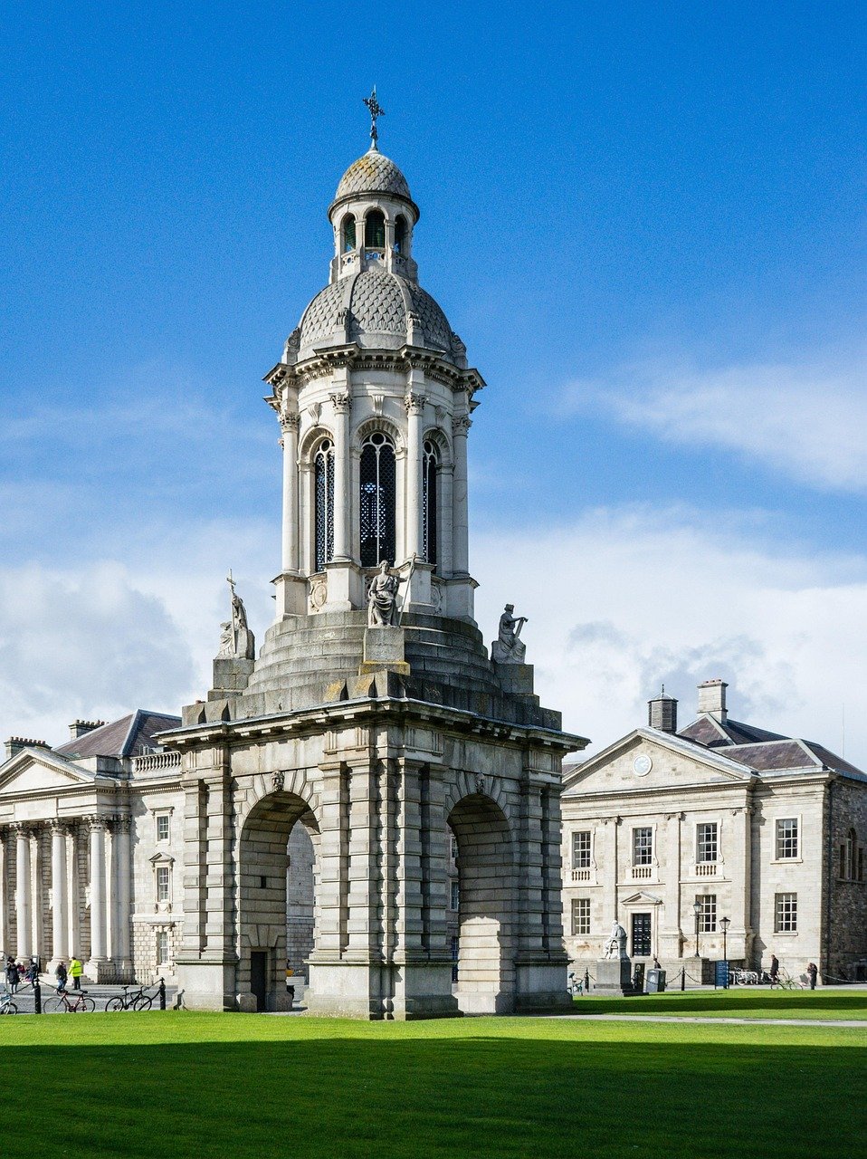 Historic stone bell tower with statues and arches at Trinity College Dublin campus under blue sky