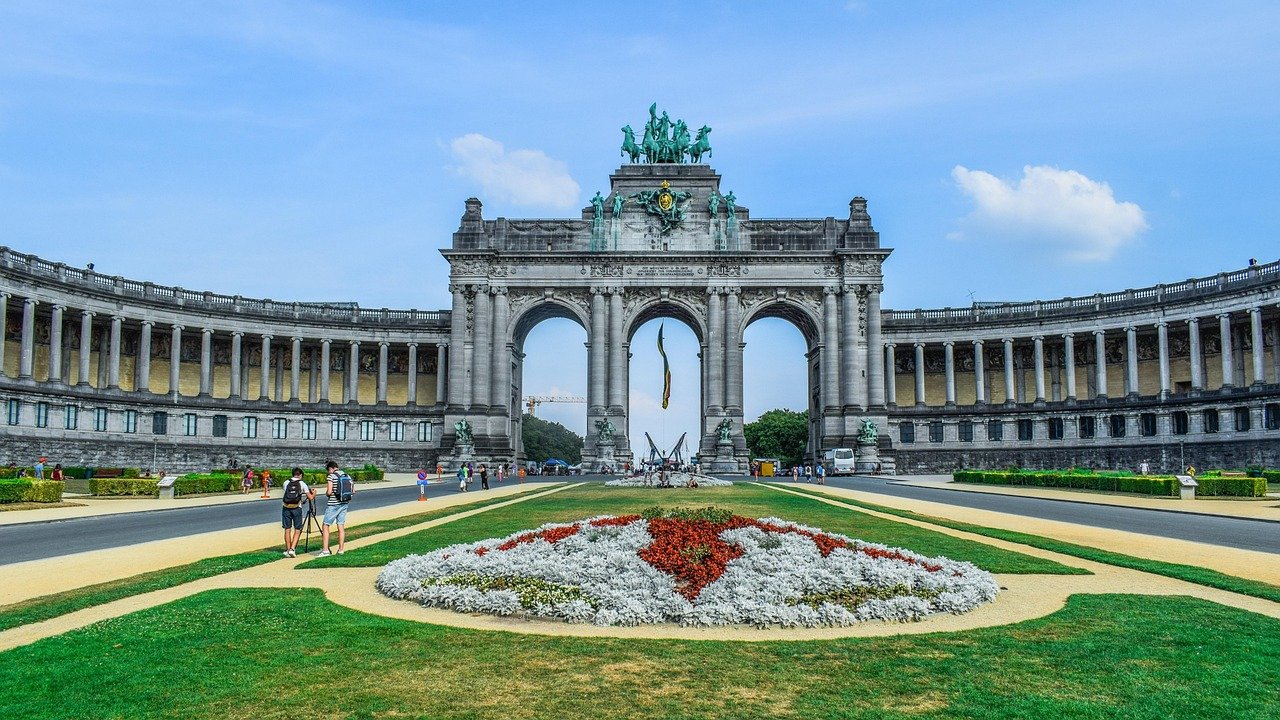Triumphal arch monument with statues and flower garden in Brussels park under blue sky