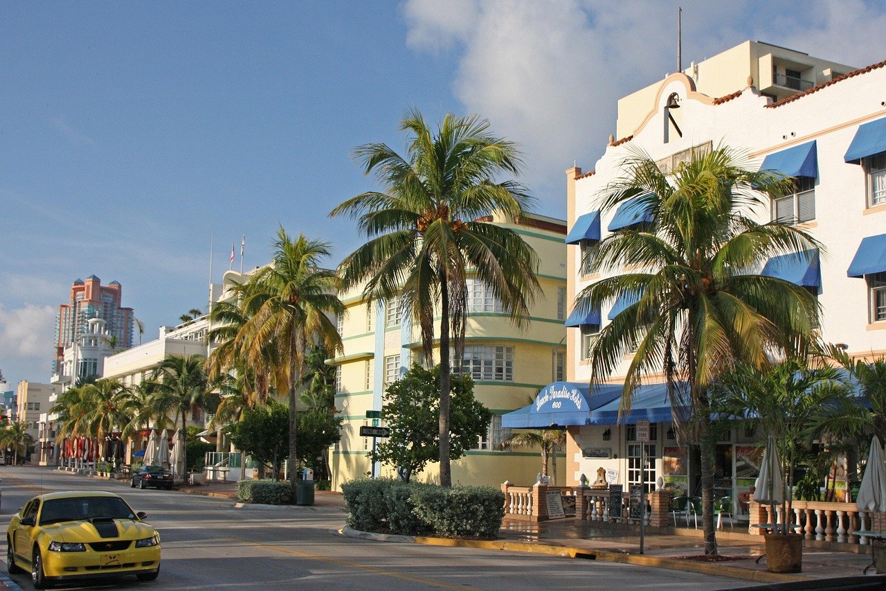 Sunny street view with palm trees, colorful buildings, and a yellow sports car in a tropical city setting
