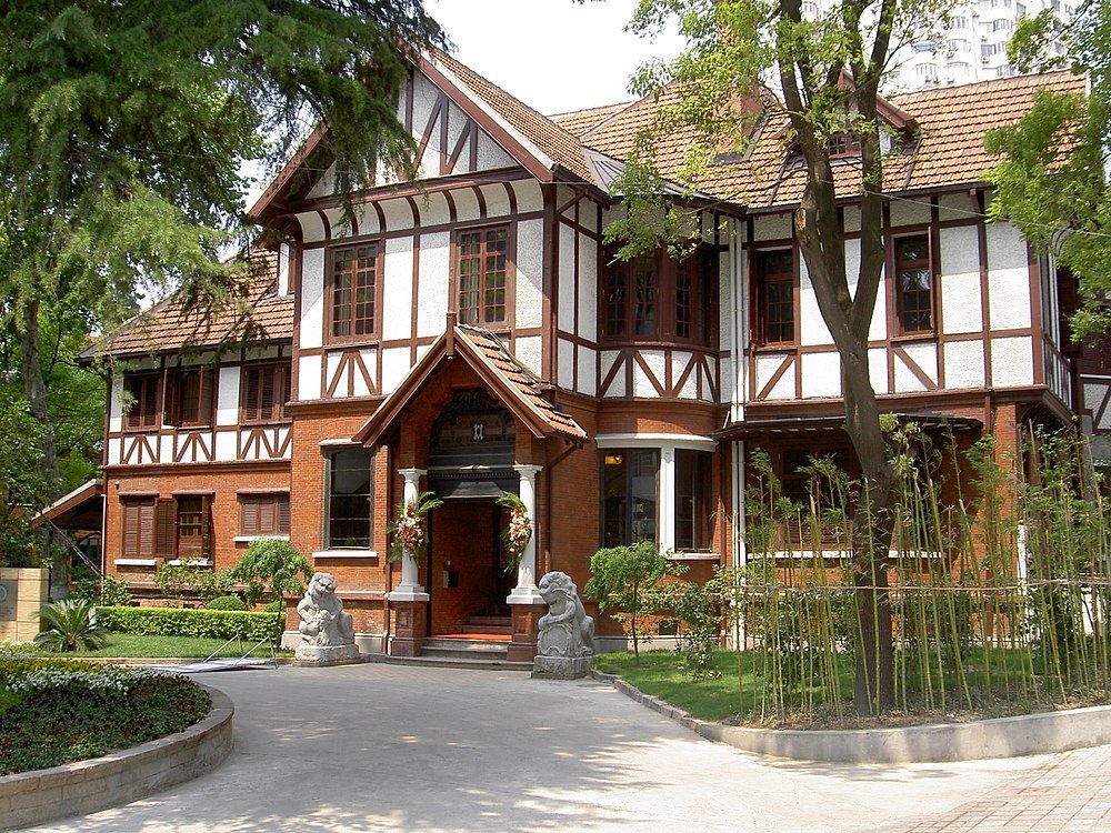 Tudor-style house with brick and timber facade Large Tudor-style house with brick and timber facade surrounded by trees and garden in sunny weather