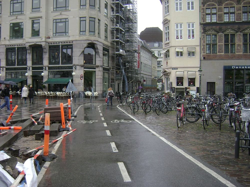 Rainy urban street with bike lane and parked bicycles Urban street scene with wet pavement, bike lane, numerous parked bicycles, and pedestrians near cafes and buildings in rainy weather