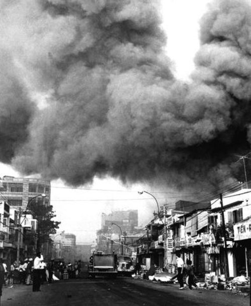 Urban street engulfed in thick black smoke from fire Thick black smoke billowing over a city street with people and vehicles during an urban fire or disaster event