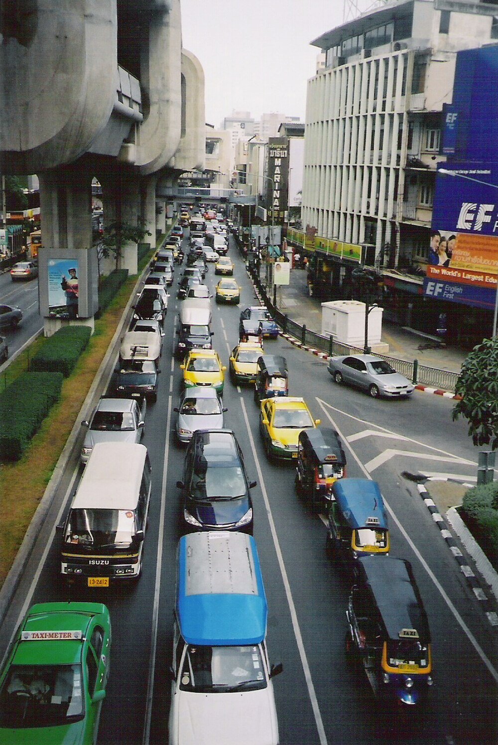 Urban street traffic with cars and tuk-tuks Busy urban street traffic with cars, taxis, tuk-tuks, and elevated train tracks in a city during daytime