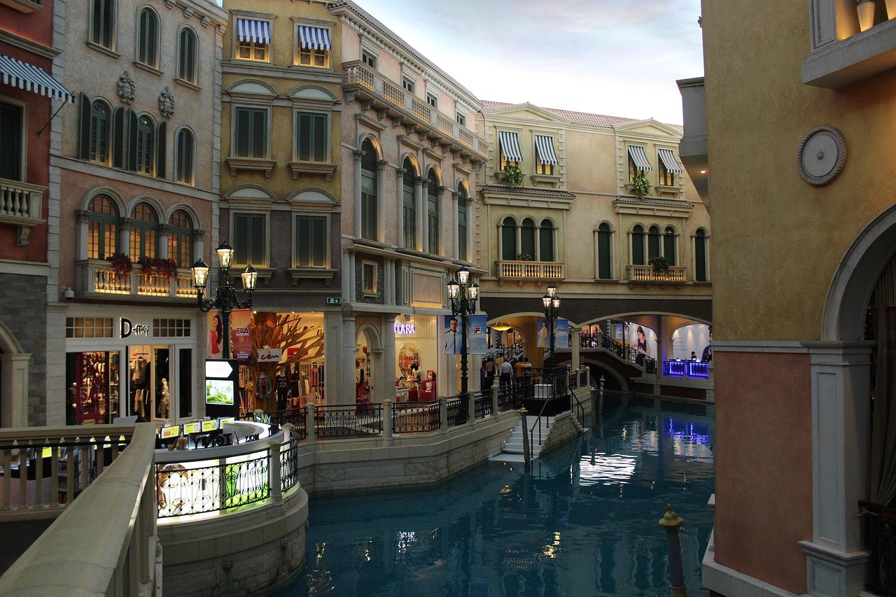 Indoor shopping mall with Venetian-style canal, bridges, and European architecture featuring shops and street lamps