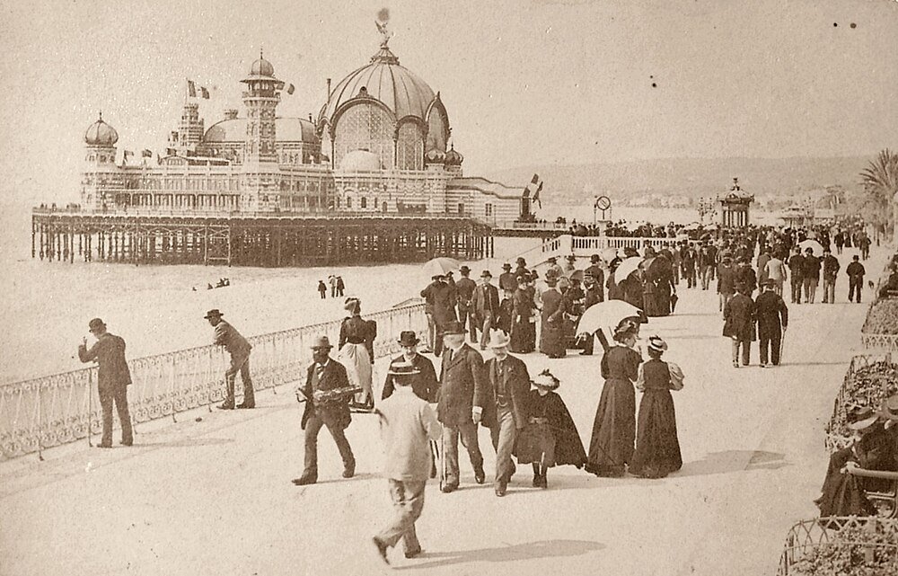 Victorian-era seaside promenade with ornate pier pavilion Vintage photo of Victorian-era people walking on a seaside promenade near a large ornate pier pavilion