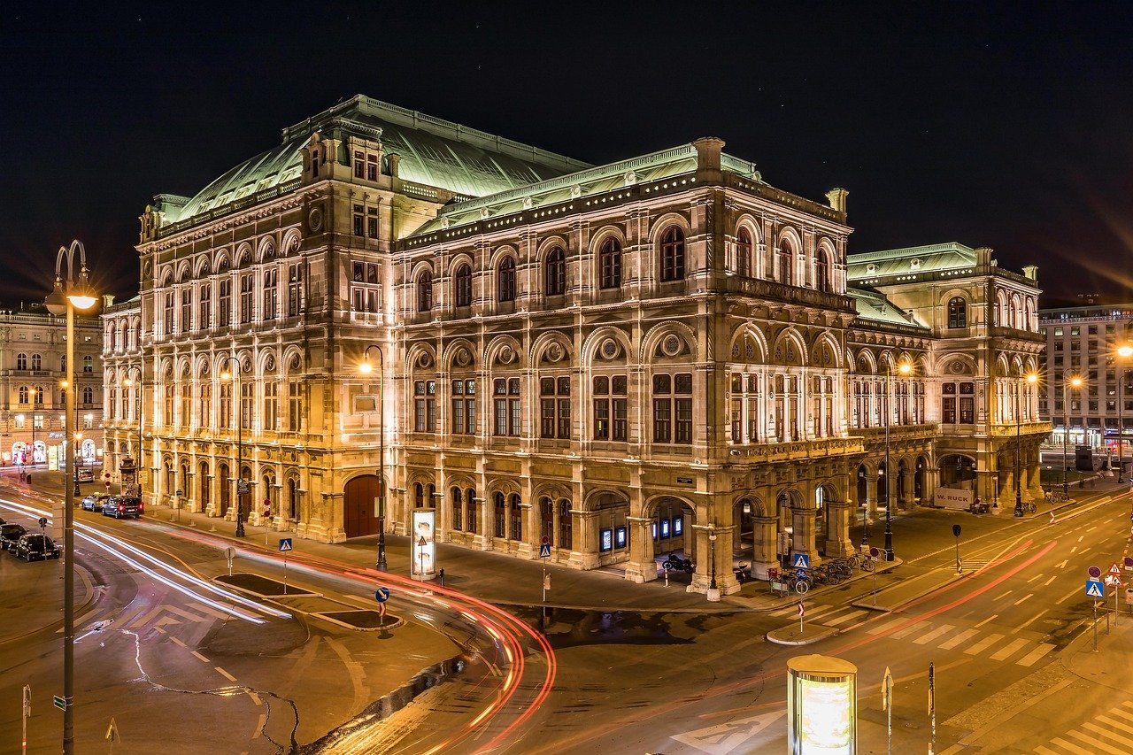 Night view of the illuminated Vienna State Opera building with light trails from passing cars on surrounding streets