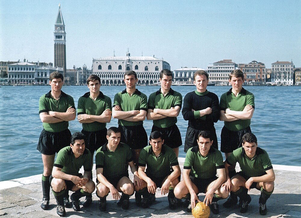 Vintage soccer team posing by Venetian waterfront Vintage soccer team in green uniforms posing by waterfront with historic Venetian buildings and bell tower in background