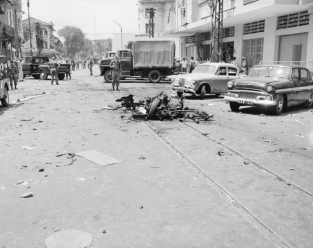 Vintage street scene with soldiers and debris Black and white photo of a street with vintage cars, debris in the middle, and soldiers standing around during a historical event