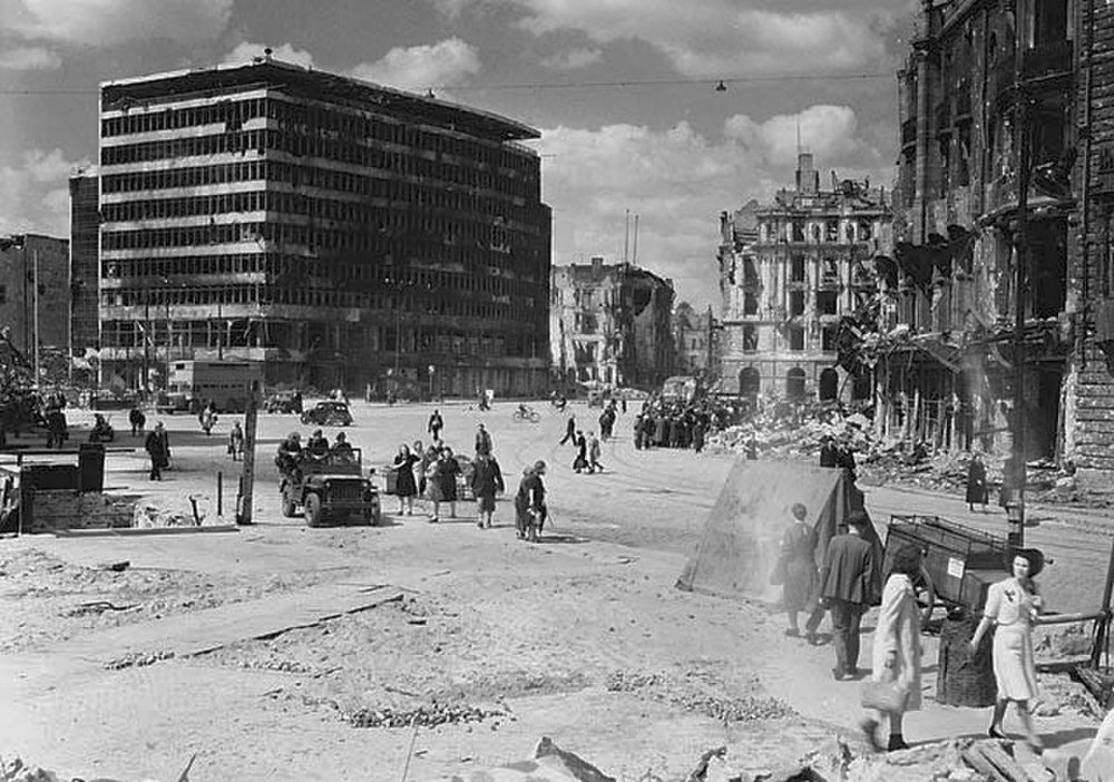 War-torn city street with damaged buildings and pedestrians Black and white photo of a war-torn city street with damaged buildings and people walking amidst rubble