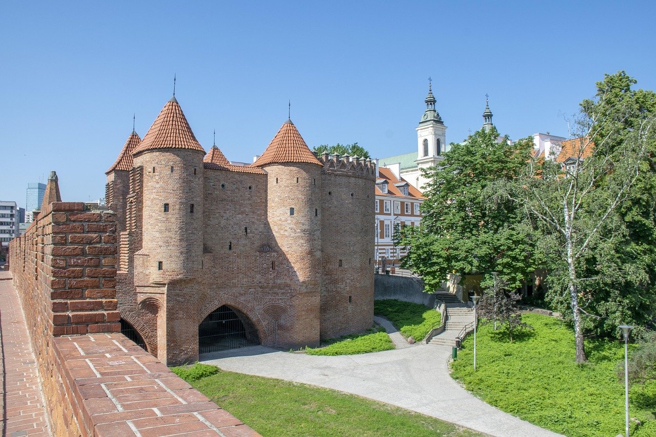 Historic brick Barbican fortress with conical roofs and city park in Warsaw, Poland under clear blue sky