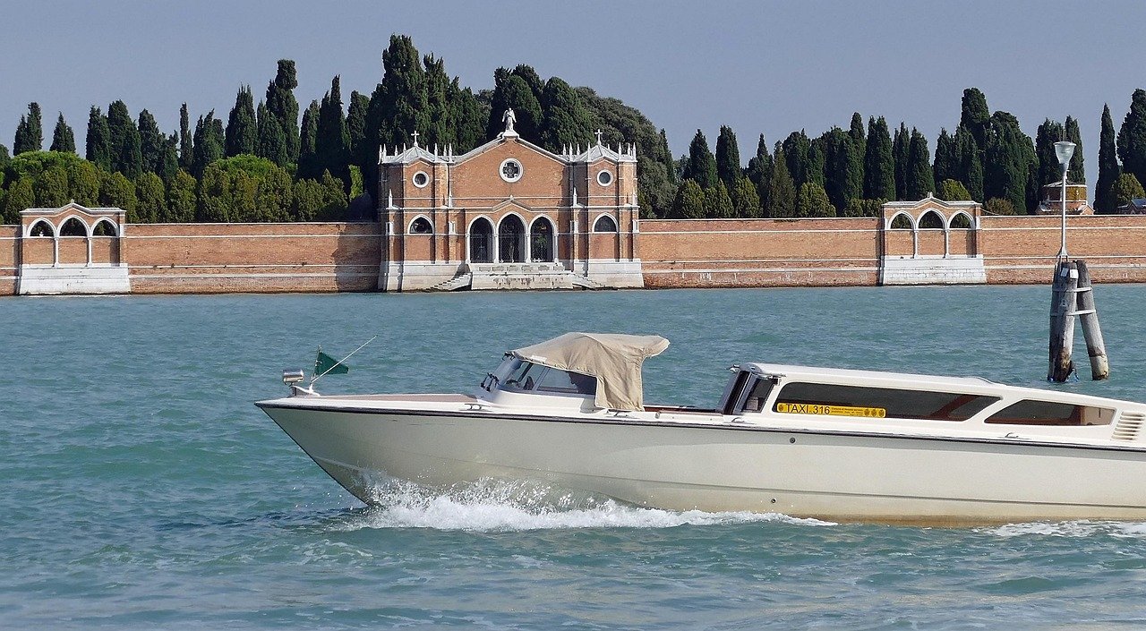 White water taxi boat cruising on turquoise water near historic brick building and tall cypress trees