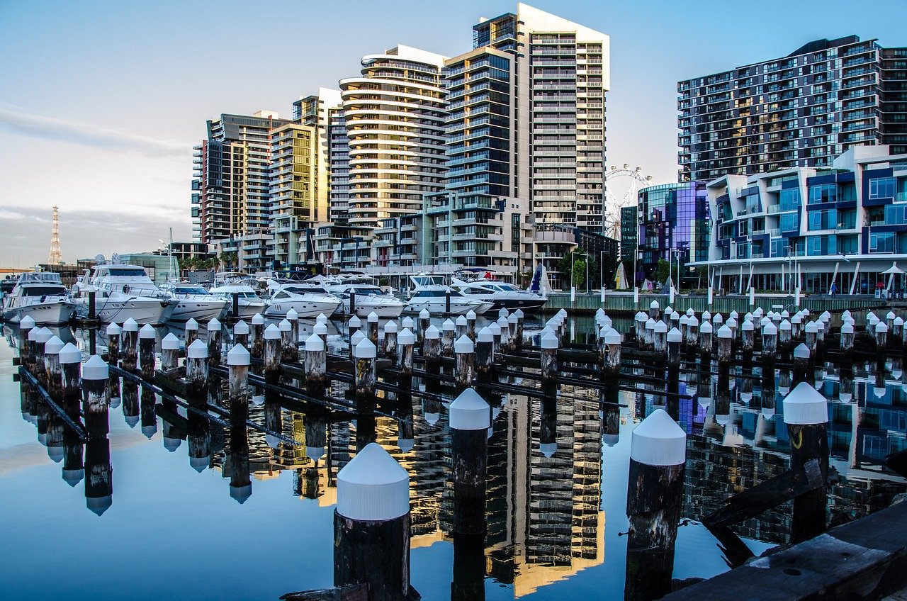 Modern waterfront marina with luxury yachts and high-rise residential buildings reflecting in calm water at sunset