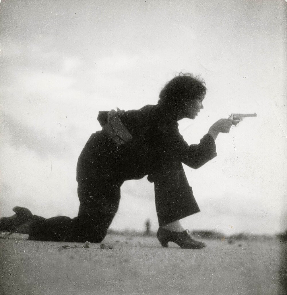 Woman kneeling and aiming a revolver pistol outdoors Black and white photo of a woman in heels kneeling and aiming a revolver pistol outdoors, vintage style