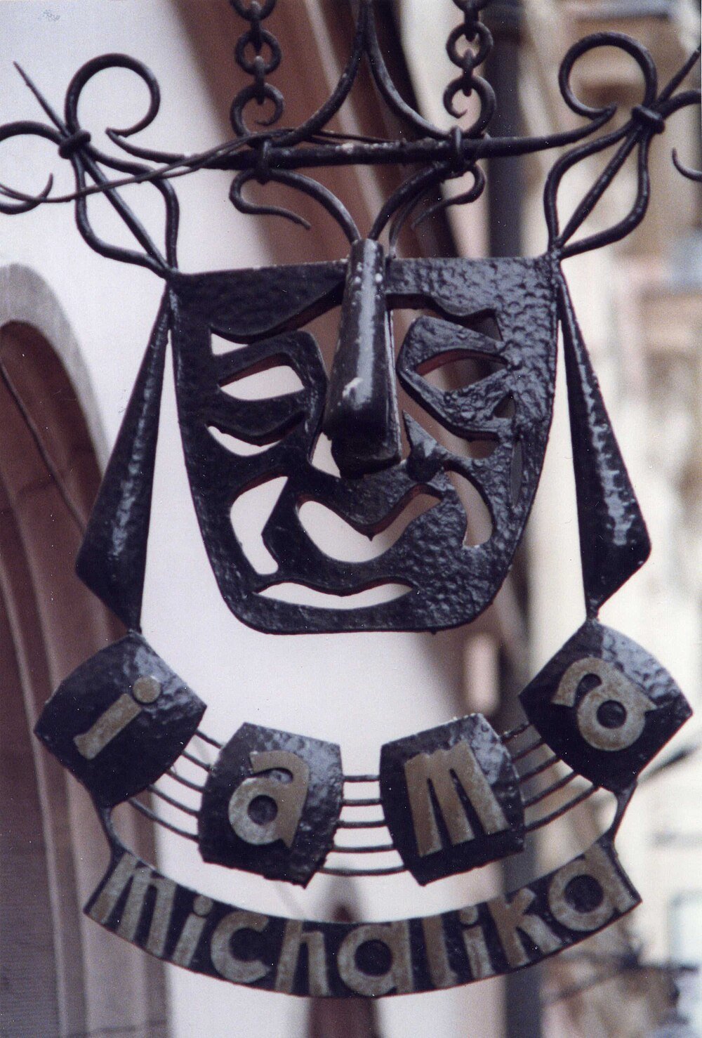 Wrought Iron Sign with Stylized Face and Text Decorative wrought iron sign with a stylized face and the words i am a michalika, artistic metalwork in a street setting