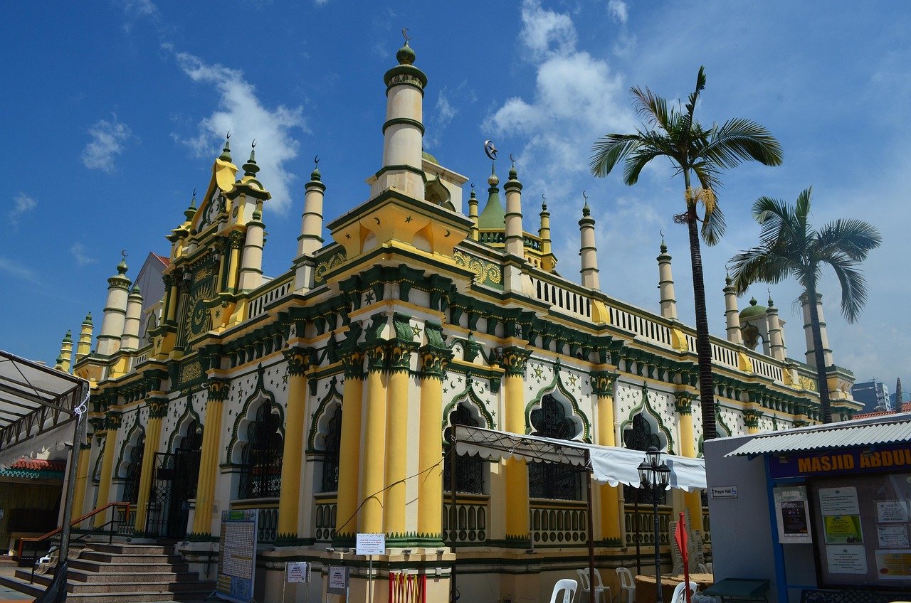 Yellow and green mosque with multiple minarets and palm trees under a clear blue sky in a sunny day