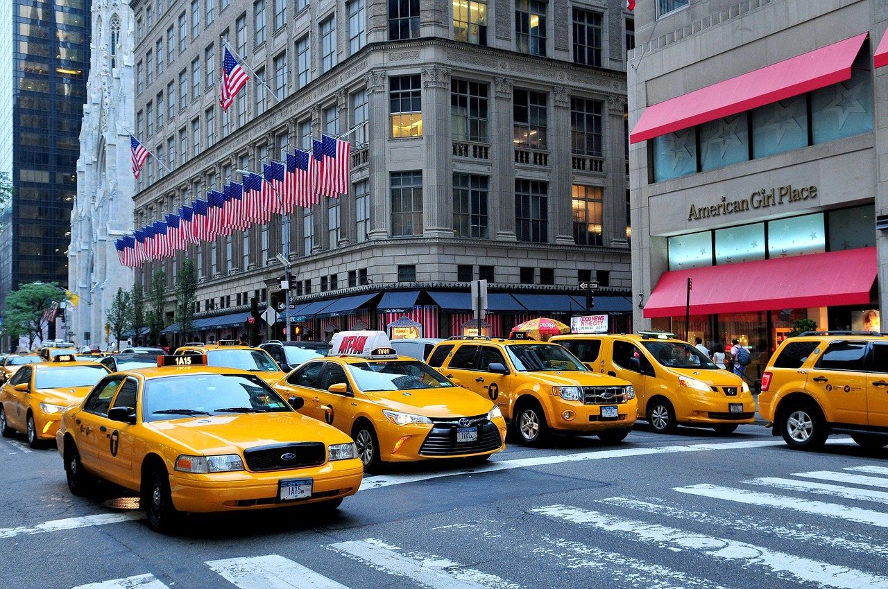 Yellow New York City taxis lined up on a busy street with American flags and tall buildings in the background
