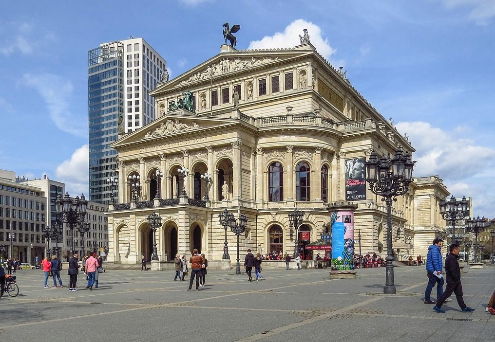 Historic Alte Oper building in Frankfurt with people walking and modern skyscraper in the background on a sunny day