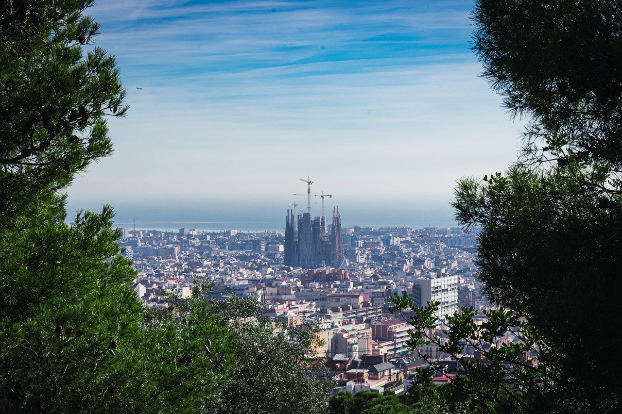 Panoramic view of Barcelona city with Sagrada Familia basilica under construction framed by green trees