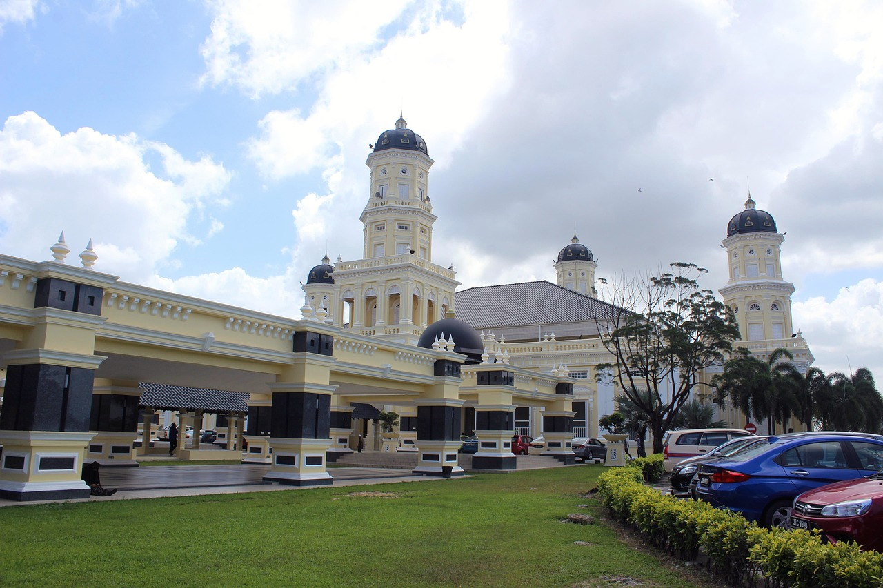 Colonial government building with clock towers and lawn Colonial-style government building with clock towers, lush green lawn, and parked cars under a partly cloudy sky