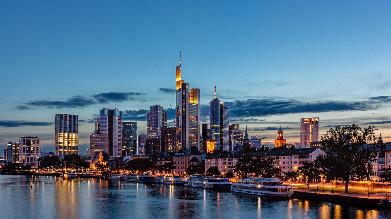 Frankfurt city skyline at dusk with river and boats Skyline of Frankfurt city at dusk with illuminated skyscrapers and riverfront boats reflecting on the water