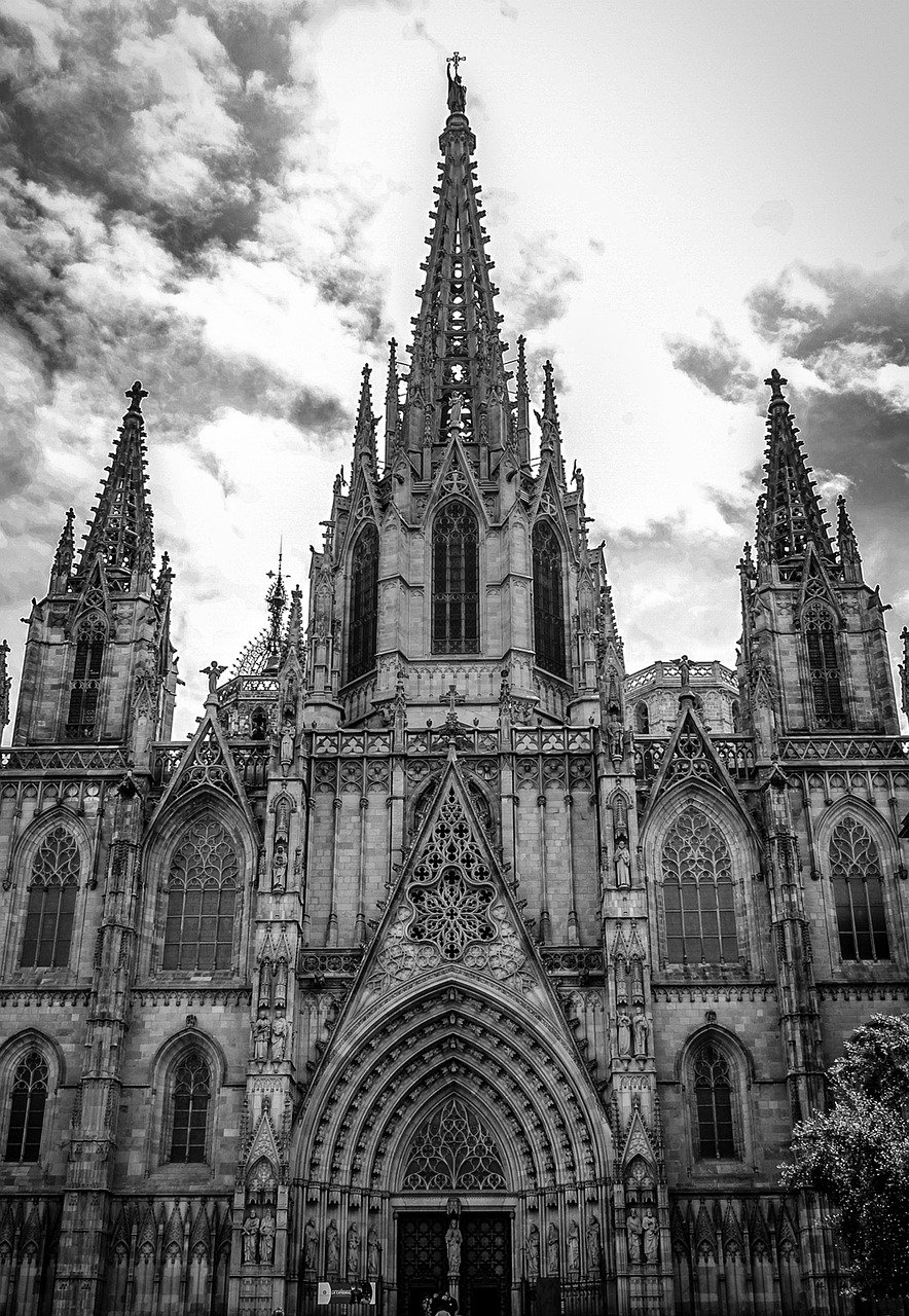 Gothic cathedral facade with intricate spires and detailed stone carvings under a cloudy sky in black and white