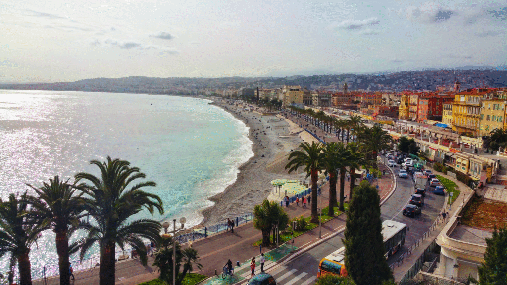 Scenic view of the Promenade des Anglais in Nice with palm trees, pebble beach, and the turquoise Mediterranean — the iconic seafront of the French Riviera