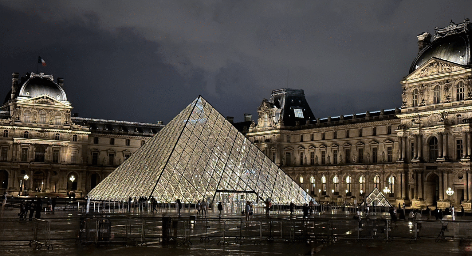 Illuminated glass pyramid entrance of the Louvre Museum at night with historic Parisian architecture in Paris