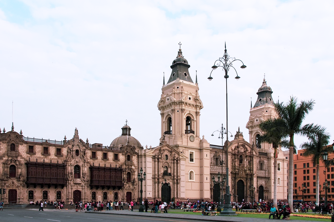 Lima Plaza Mayor Cathedral and Government Palace Historic colonial cathedral and government palace in Lima's Plaza Mayor with tourists and palm trees under cloudy sky