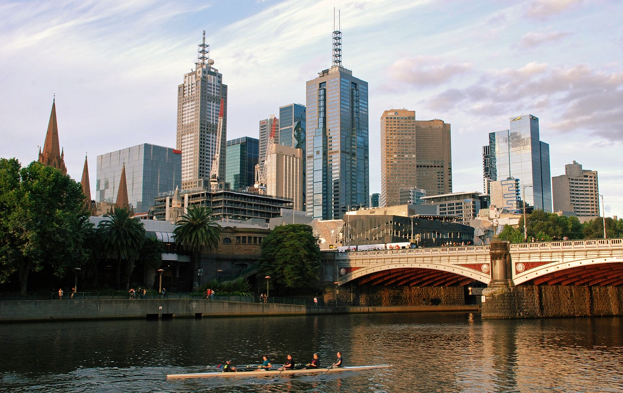 Melbourne skyline with Yarra River and rowers Melbourne city skyline with Yarra River, modern skyscrapers, historic buildings, and a rowing team on the water at sunset