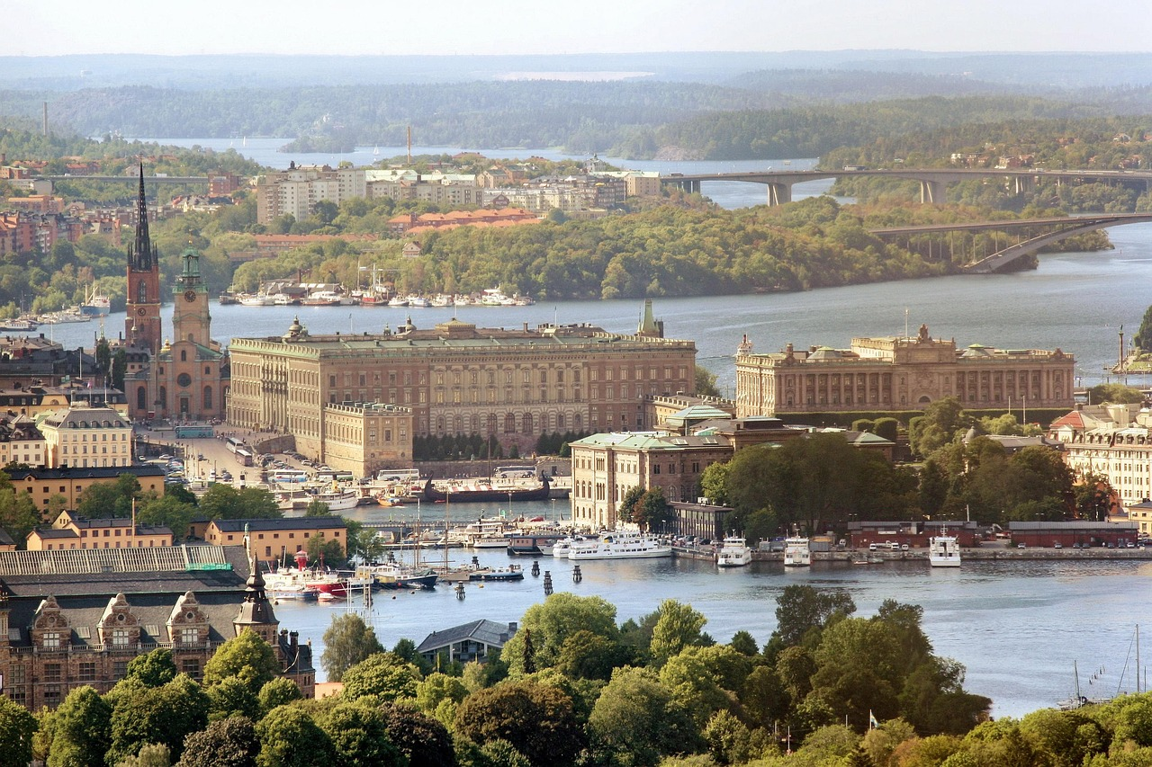 Scenic view of Stockholm city with historic buildings, waterfront, boats, and lush greenery under clear sky