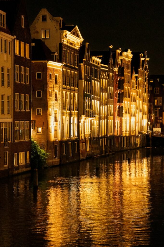 Historic Amsterdam canal houses illuminated at night with reflections in the water, capturing the city's nightlife atmosphere