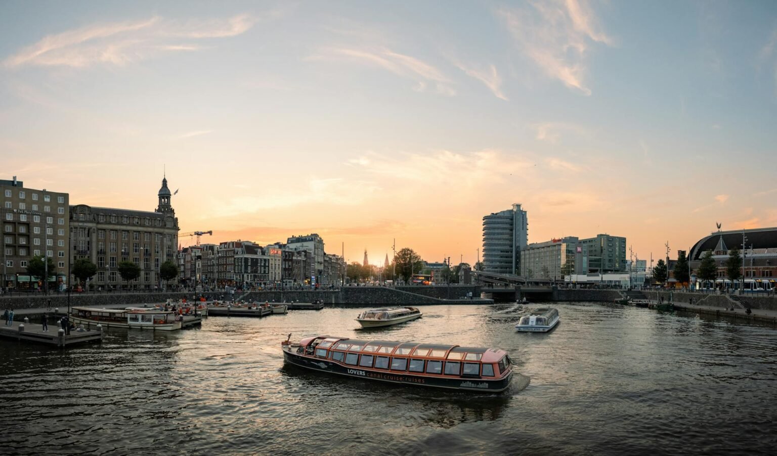 Sunset over Amsterdam's historic canals with tour boats and the iconic gabled canal-house cityscape in the background