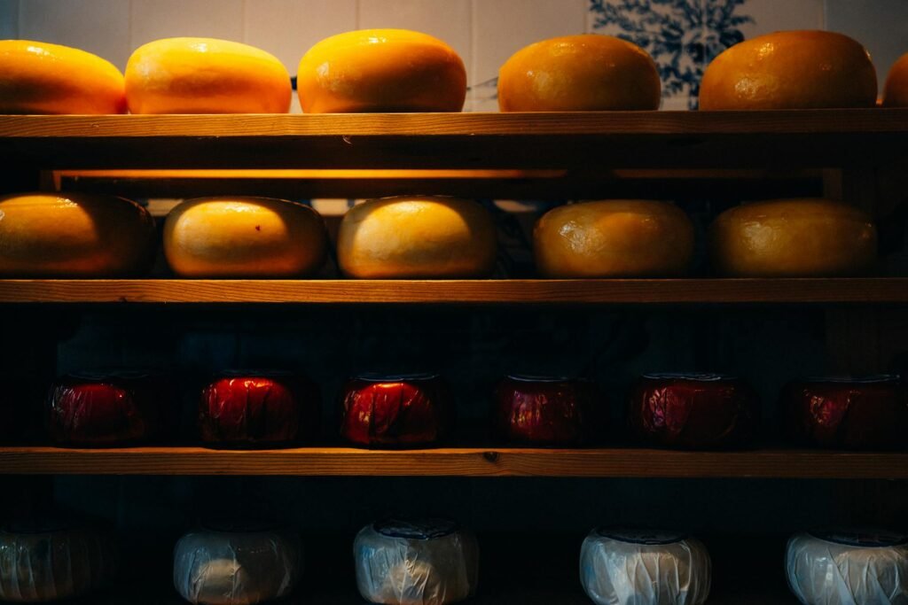 Rows of traditional Dutch cheese wheels (Gouda and Edam) displayed on wooden shelves in an Amsterdam shop