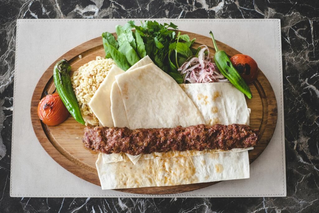 Savory Adana kebab served on a wooden plate with fresh greens, tomatoes, and traditional flatbread