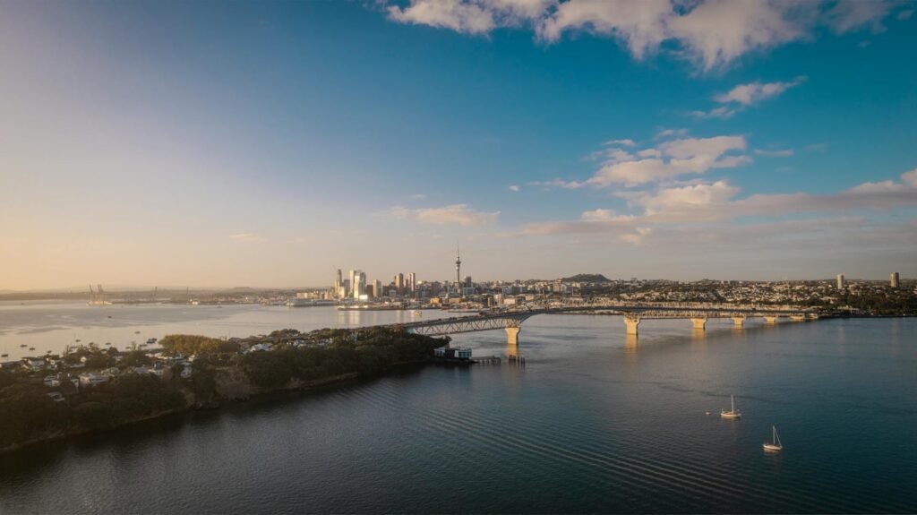 Stunning aerial view of Auckland's city skyline and the Auckland Harbour Bridge at sunset — the iconic infrastructure connecting central Auckland to the North Shore across the Waitematā