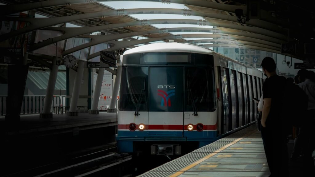 A BTS Skytrain arriving at an elevated Bangkok metro station platform with passengers waiting