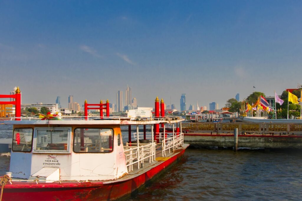 A Chao Phraya River ferry docked near a Bangkok pier with the city skyline in the background