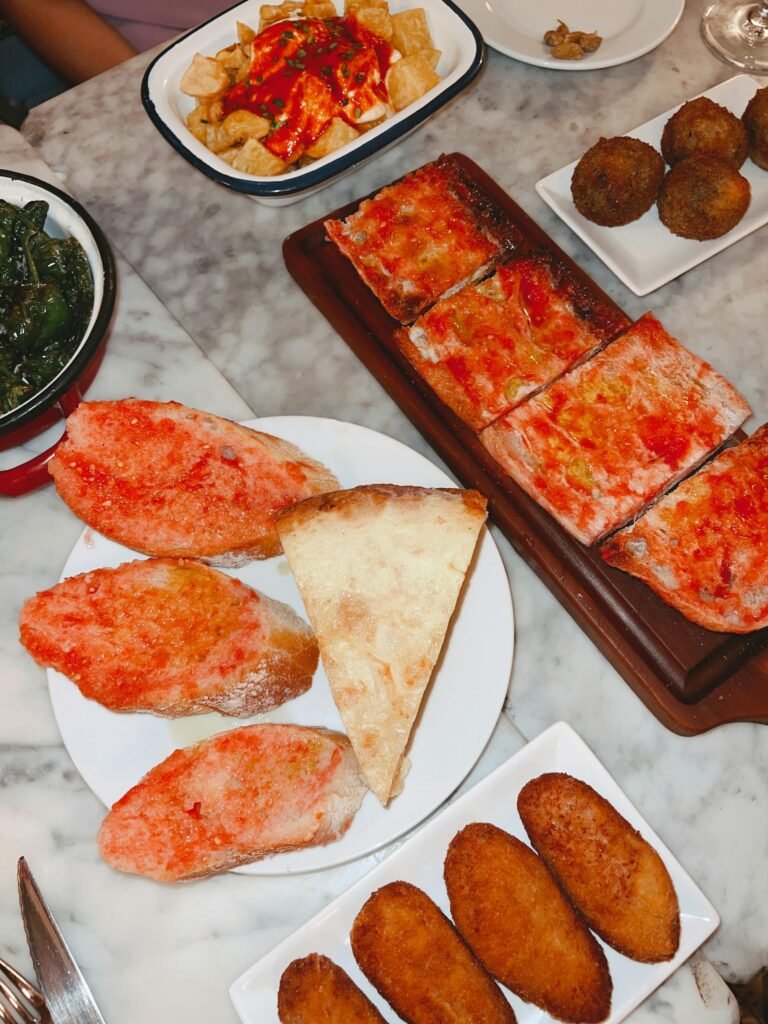 A vibrant spread of Spanish tapas including patatas bravas, pa amb tomàquet, and croquettes on a marble table in Barcelona