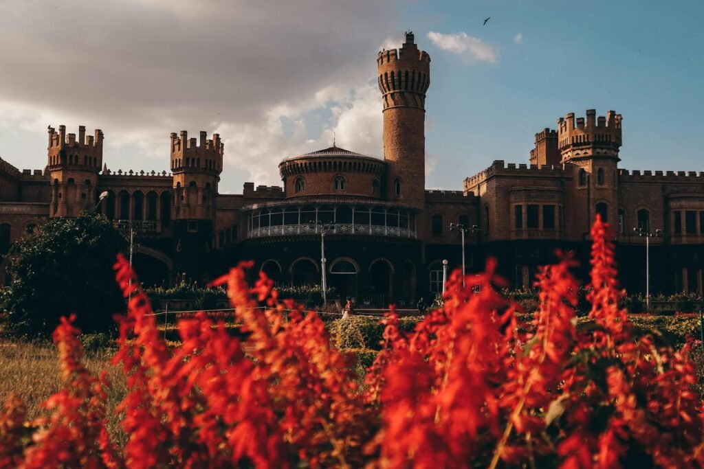 The 1887 Bangalore Palace — Bengaluru's Tudor-Gothic Wodeyar royal residence inspired by Windsor Castle — framed by vibrant red flowers under a partly cloudy sky