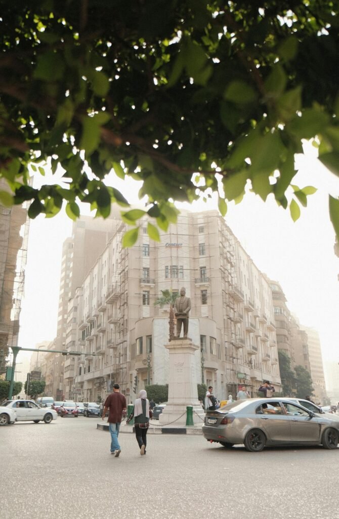 A bustling Cairo intersection with people, vehicles, and a prominent landmark statue, capturing the daily energy of central Cairo