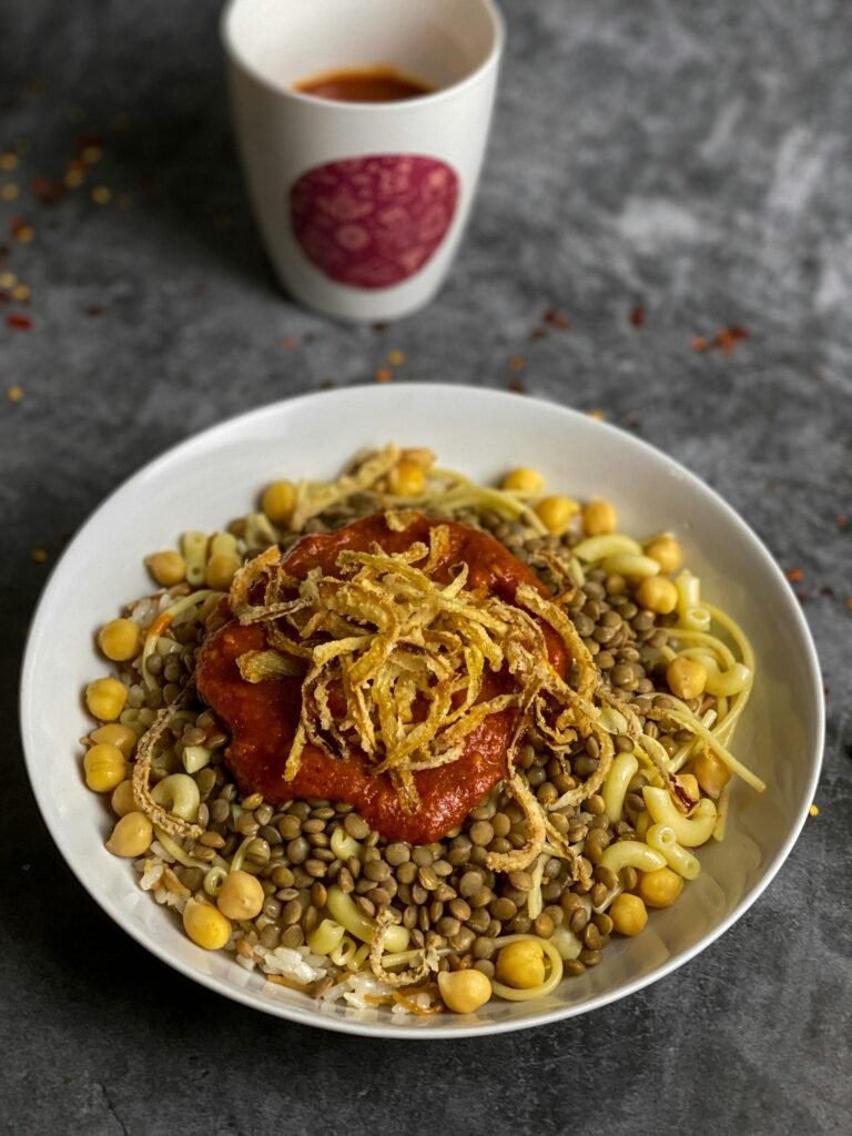 A close-up of koshari, Egypt's signature street dish of pasta, rice, lentils, and chickpeas topped with tomato sauce and crispy fried onions