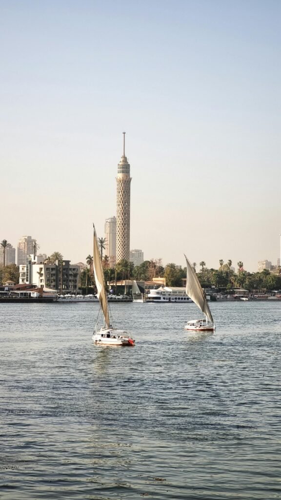Wooden feluccas with white sails on the Nile River in central Cairo, with the Cairo Tower rising on the riverbank