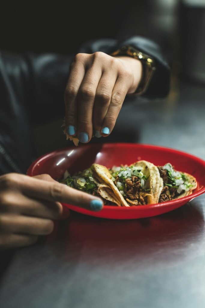 Hand squeezing a slice of lime over freshly prepared Mexican tacos with cilantro and onions