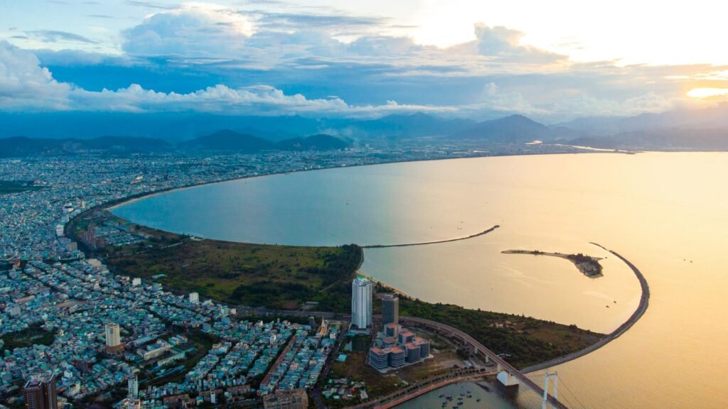 Aerial sunset view of Da Nang Bay — the curved coastline of central Vietnam with the city center, Han River, and Truong Son mountain range framing the harbor
