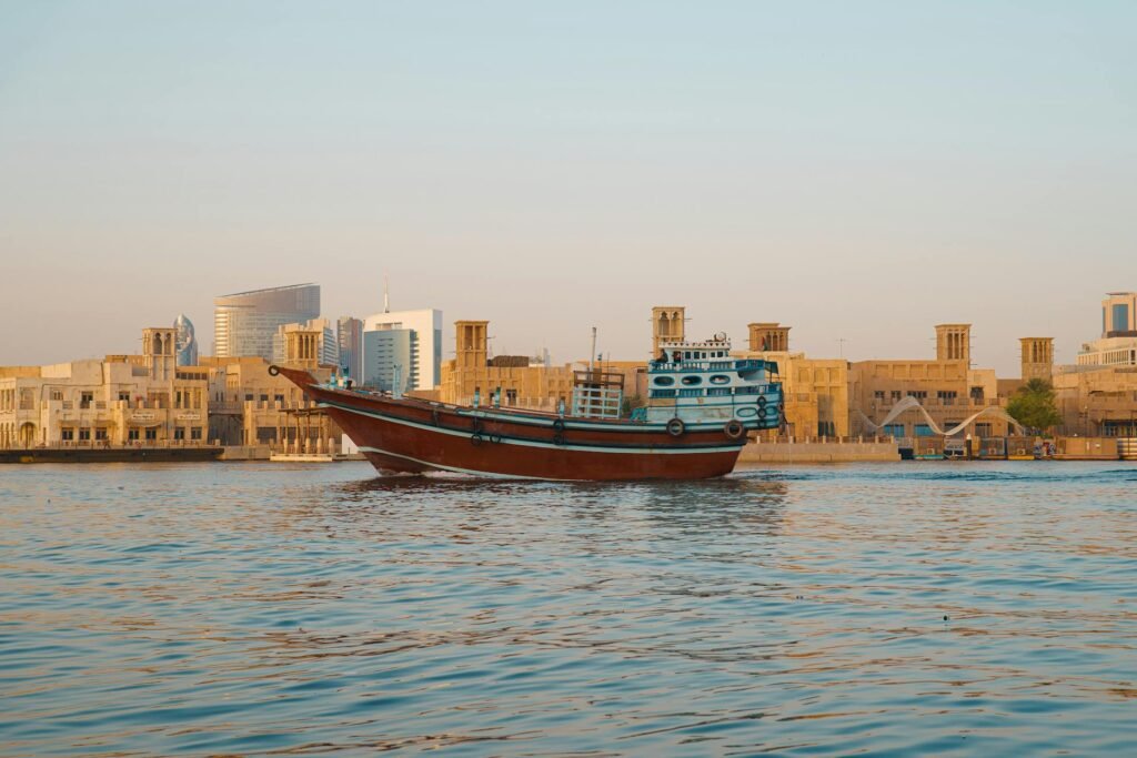 A traditional wooden dhow boat sailing through Dubai Creek with heritage architecture in the background