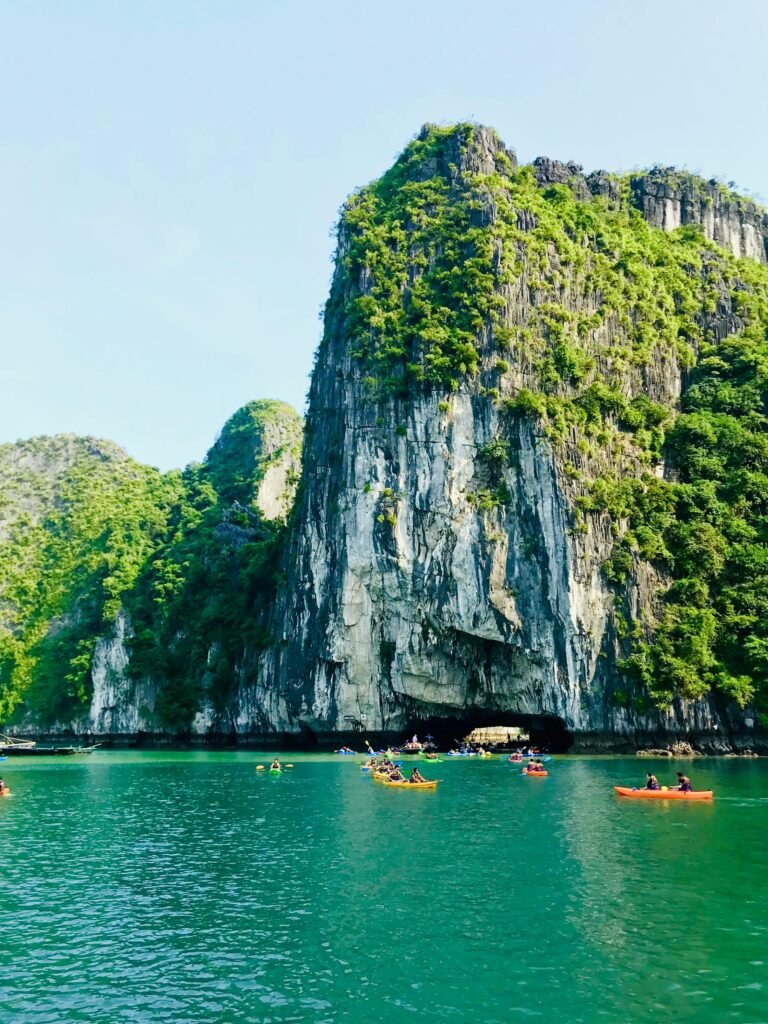 Kayakers paddling through scenic limestone cliff formations in Ha Long Bay — the increasingly regulated but still iconic on-water adventure experience
