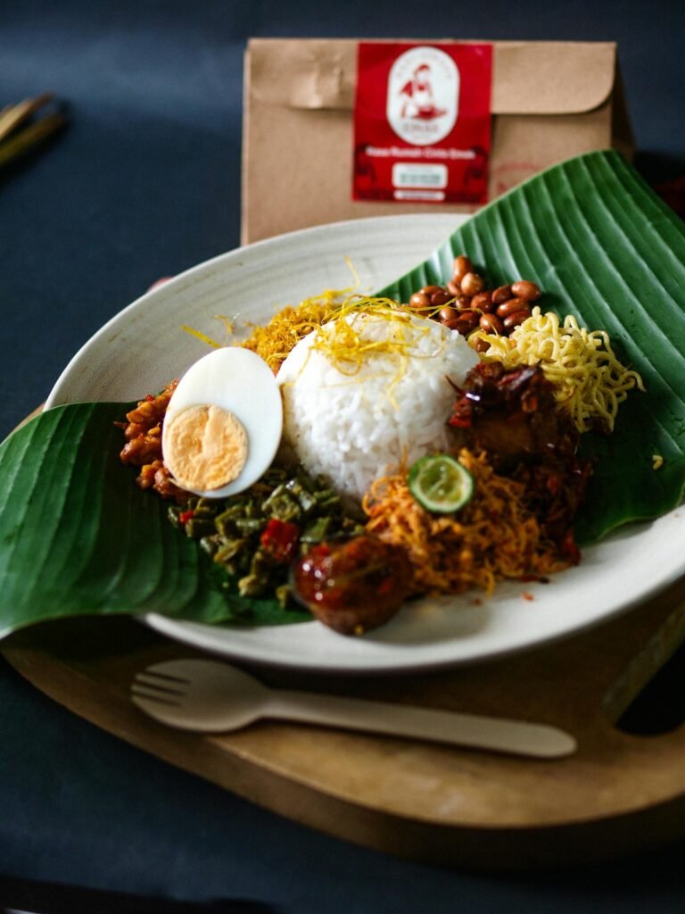 Traditional Malaysian nasi lemak served on a banana leaf with sambal, anchovies, peanuts, egg, and accompaniments