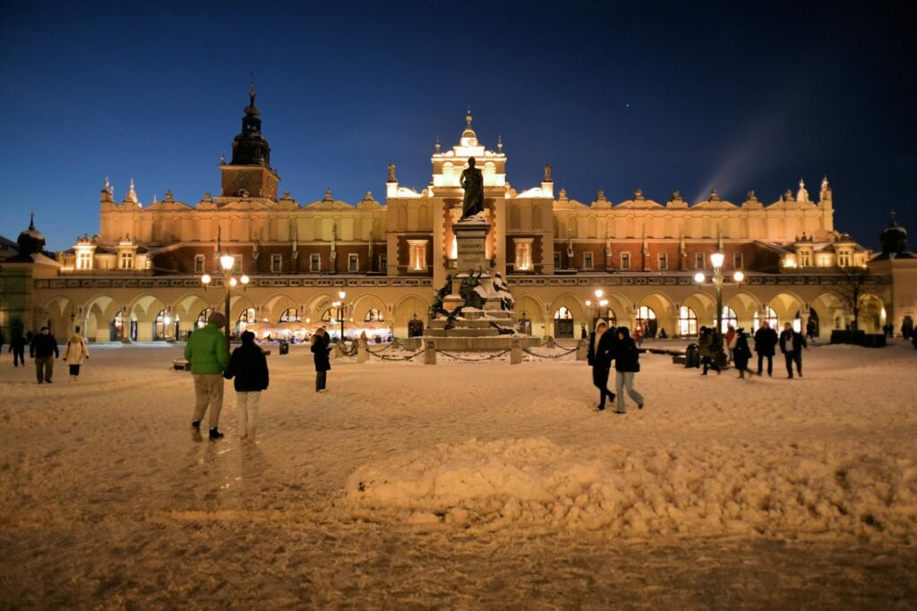 Illuminated Sukiennice Cloth Hall and Mickiewicz Monument in Krakow at night covered in snow
