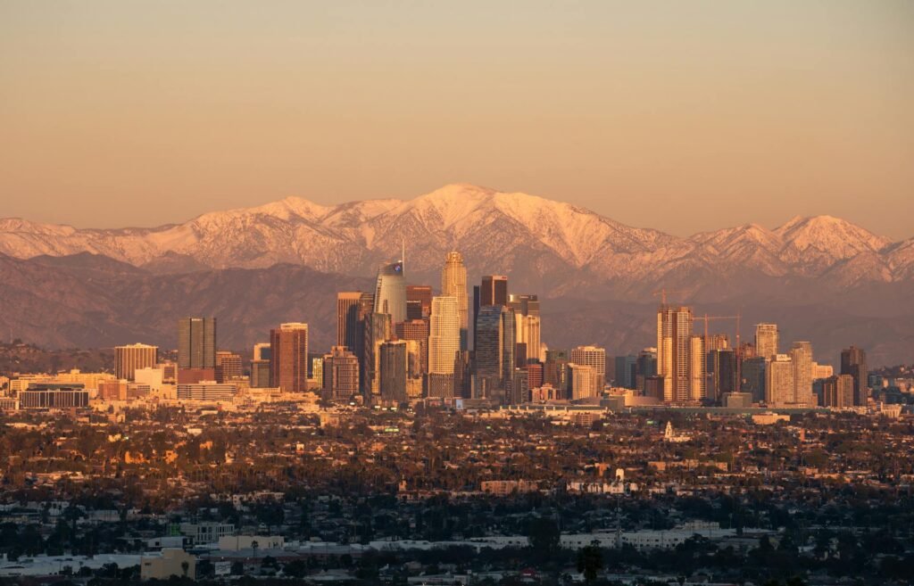 Los Angeles skyline at golden hour with snow-capped San Gabriel Mountains visible in the distance