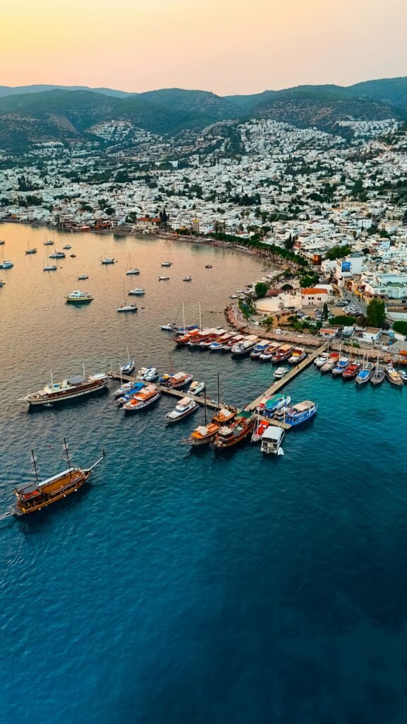 Bodrum harbor at sunset within Muğla Province — wooden Turkish gulets and traditional boats moored against the historic castle and whitewashed Aegean town silhouette